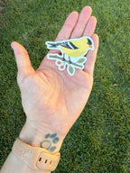 American Goldfinch sticker resting in an open palm outdoors against green grass